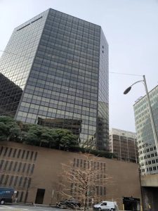 Tall black-glass office skyscraper on a city street, with trees lining the curb and a street lamp nearby.